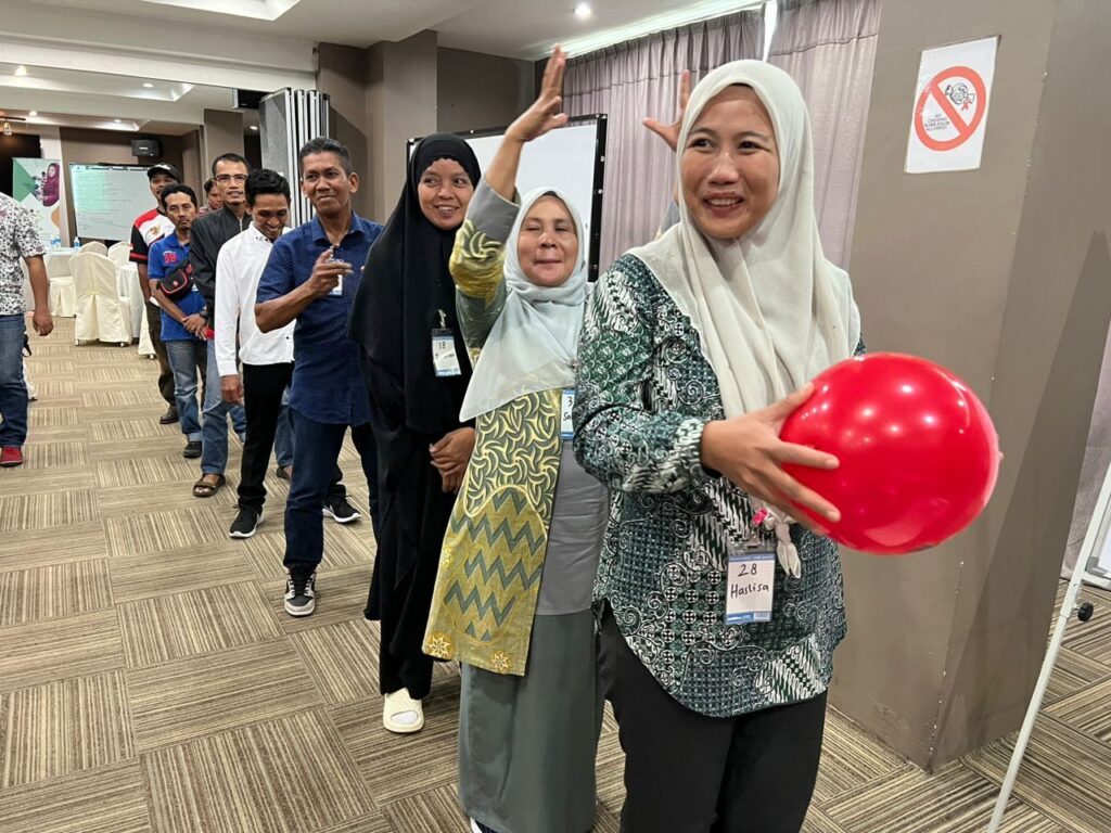 People stand in a line smiling, the person in front is holding a red baloon