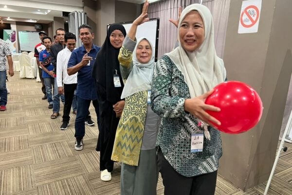 People stand in a line smiling, the person in front is holding a red baloon